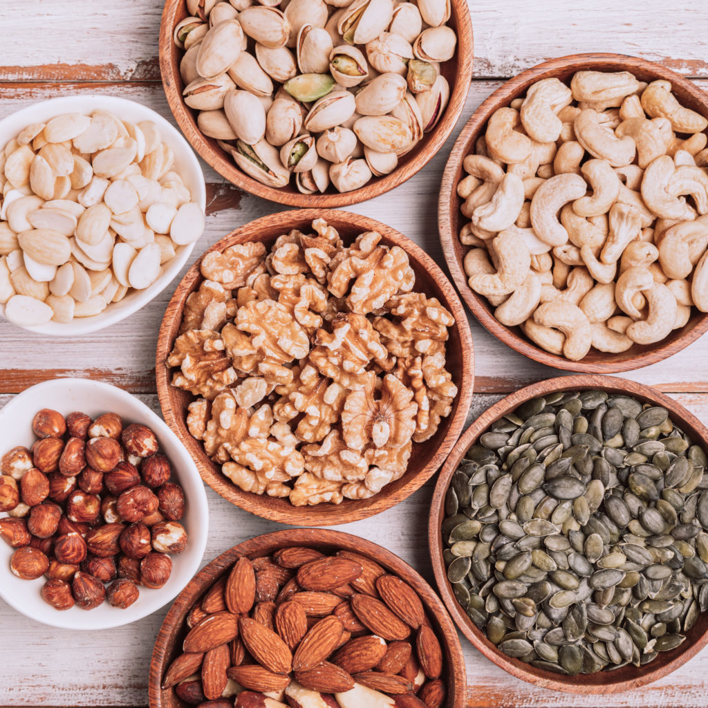 Different kind of nuts in wooden bowls such as cashew nuts, hazelnuts, walnuts, blanched almonds, brasil, roasted pistachios, pumpkin seeds. Healthy snack. Top view, shoot on wooden background