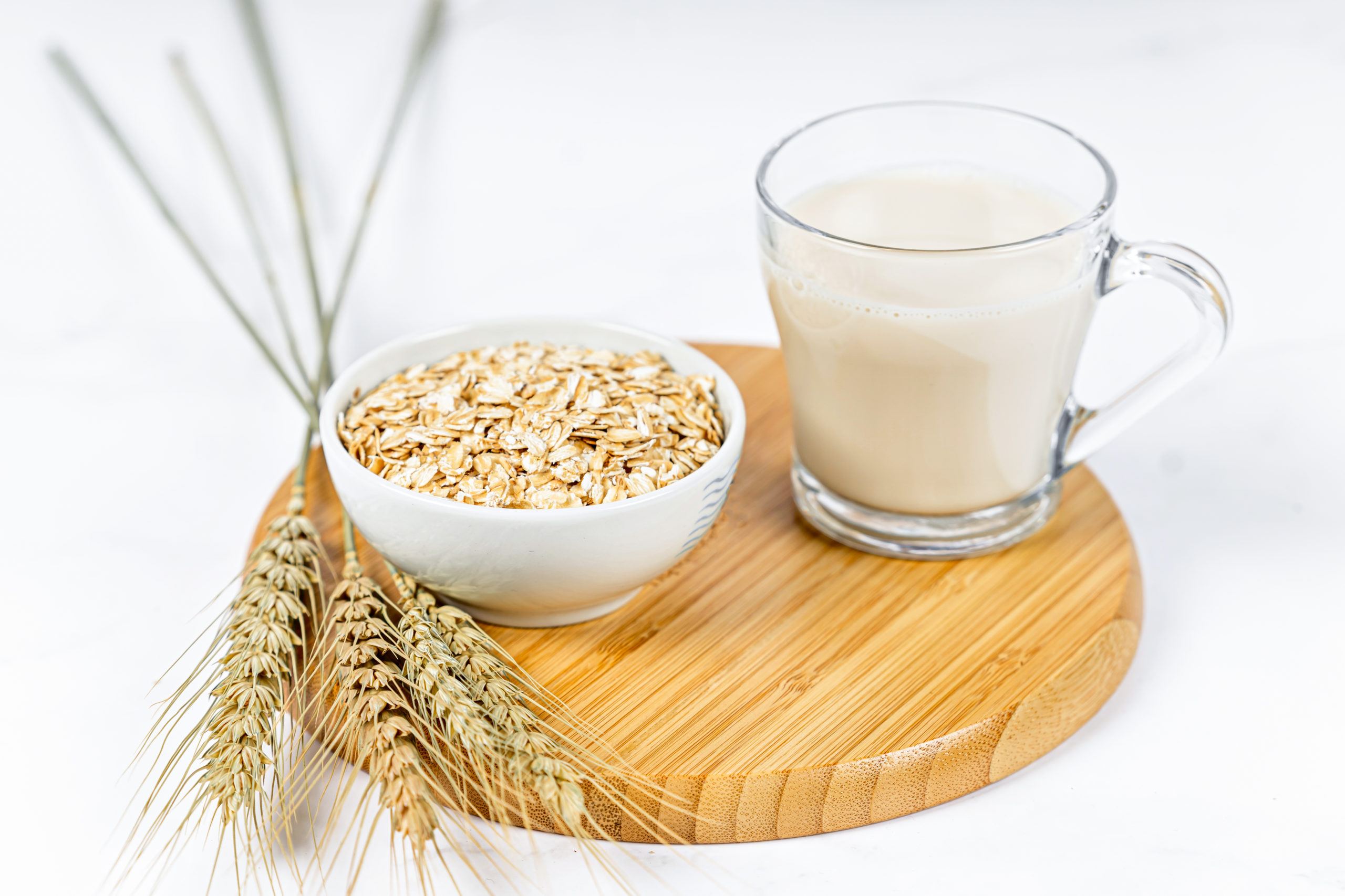 Glass of oat milk with oat flakes on white wooden background.