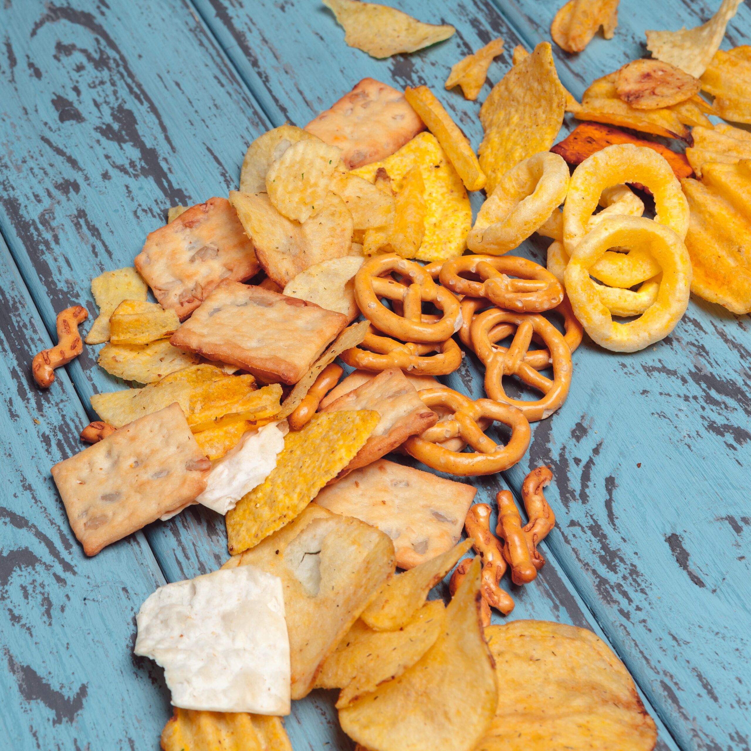 Salty snacks. Pretzels, chips, crackers on wooden background. Unhealthy products